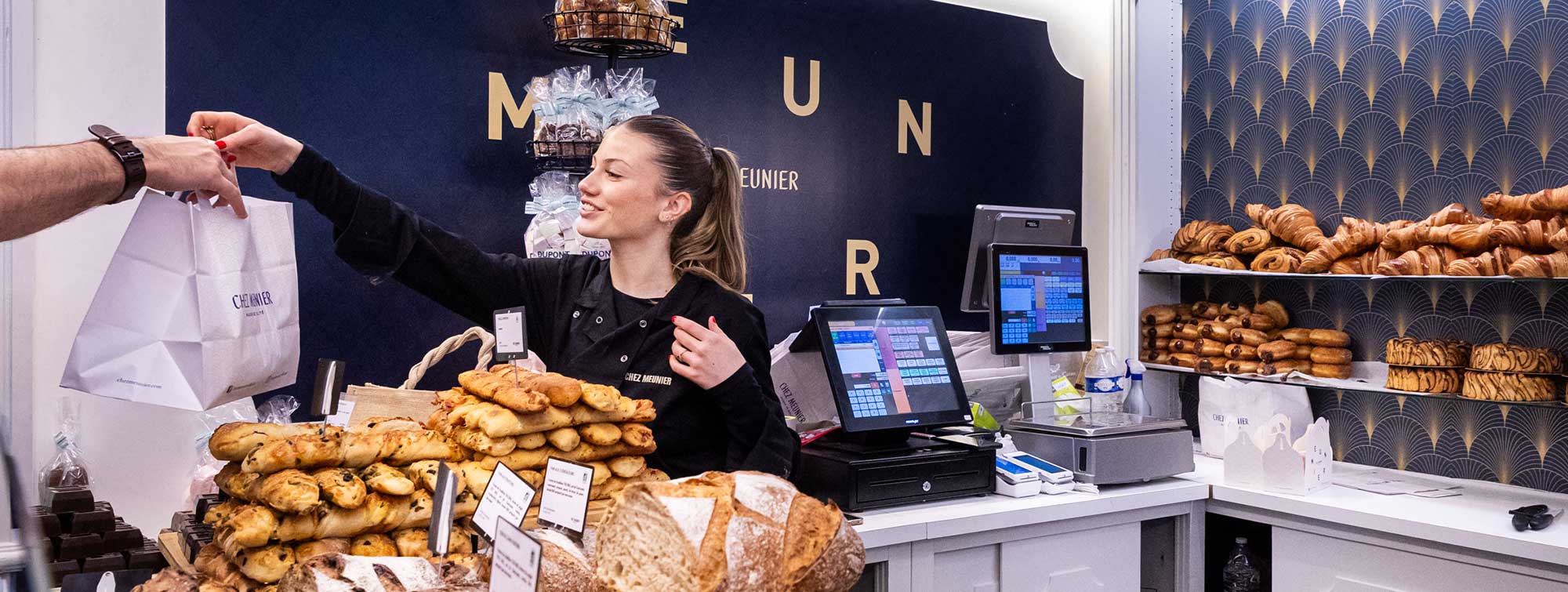 Vue sur un stand avec des viennoiseries et l'exposant qui tend le sac à l'acheteur. 
