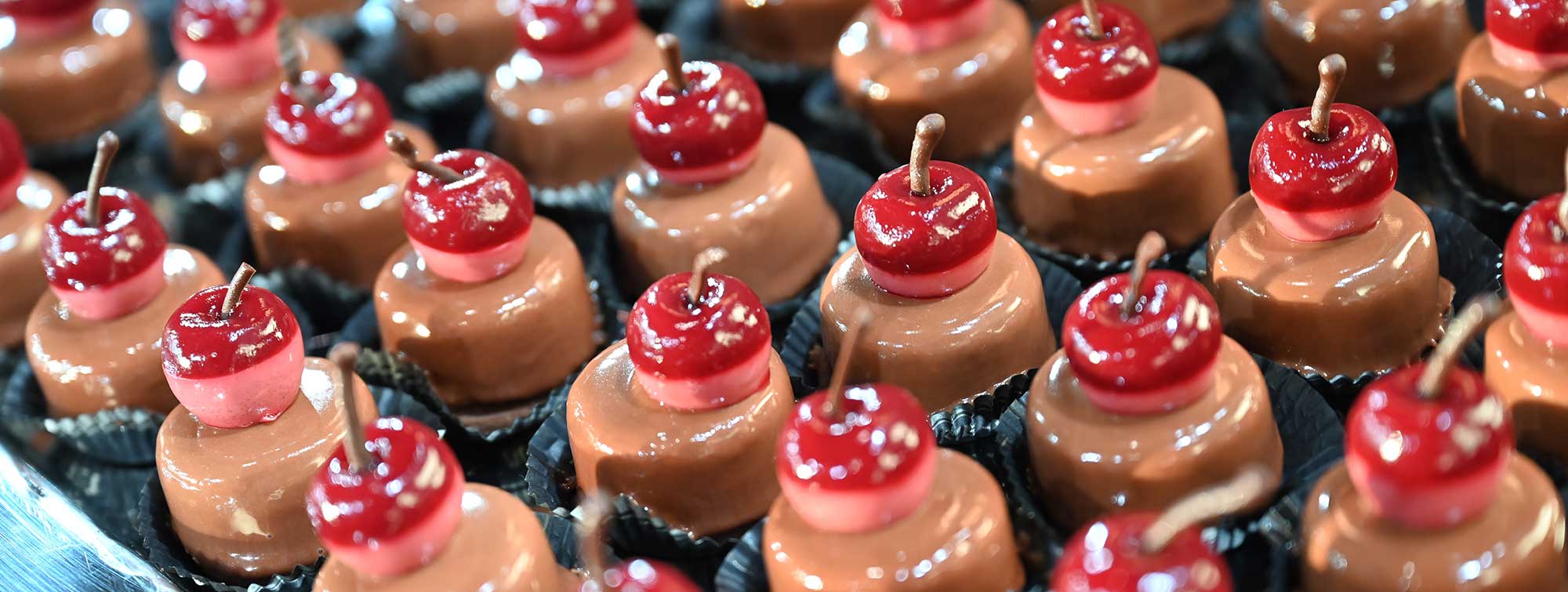 Chocolats individuels garnis de cerises rouges disposés en rangées. 