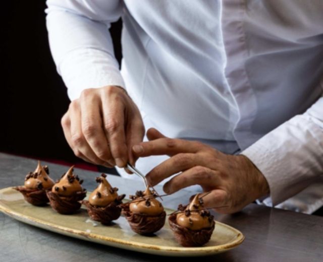Pastry chef carefully decorating chocolate creations arranged on a serving platter