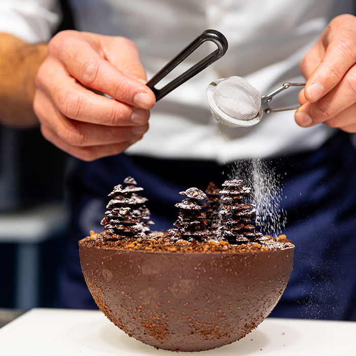 Zoom in on a pastry depicting a forest of fir trees sprinkled with powdered sugar.